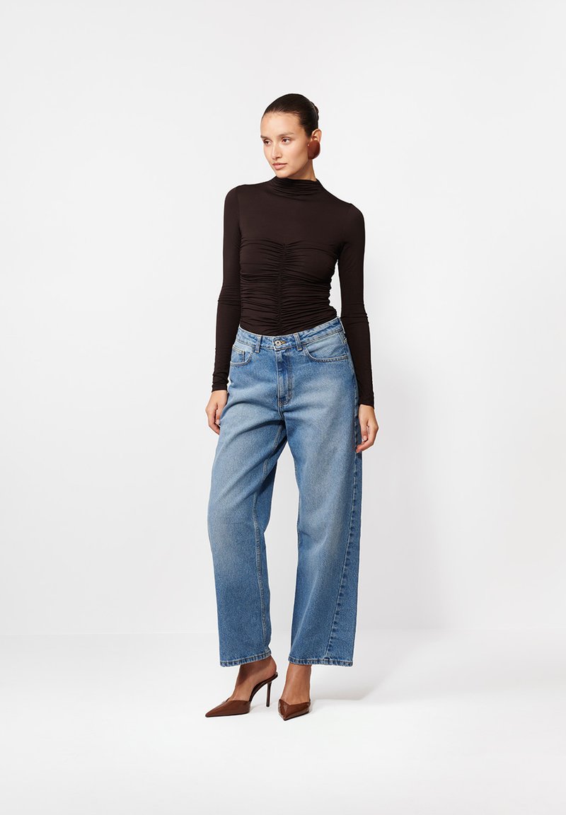 Czarny bluzka z długim rękawem z marszczeniami w połączeniu z jasnoniebieskimi spodniami z wysokim stanem, podkreślona brązowymi czółenkami na obcasie.