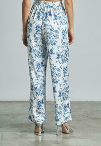 Pantalons à motif floral en blanc et bleu avec une taille élastique. Associés à des chaussures à talons hauts en argent avec un talon géométrique.