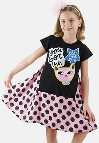 Robe noire à manches courtes avec jupe à pois roses et impression graphique de chat. Comprend les textes "Tu peux le faire !" et "Que des bonnes ondes !" en accents colorés.