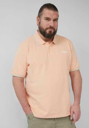 Polohemd in hellem Pfirsich mit kontrastierenden blauen Kragenstreifen. Kurze Ärmel, Knopfleiste und Emblem auf der linken Brust.