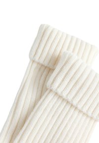 Ribbed cremede sokker med en tyk manchet, lavet af et blødt, tekstureret stof, der fremviser lodrette striber og et hyggeligt udseende.