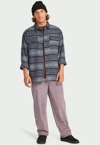 Men's button-up shirt in blue and green patterned fabric; paired with light purple corduroy pants; black sneakers; knit beanie.