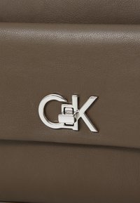 Borsa in pelle marrone con texture, caratterizzata da una chiusura a scatto in metallo argento con logo CK. Il design presenta linee pulite e una superficie liscia.