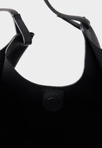 Fekete bőrből készült nagy táska, amely texturált külsővel, széles nyitott felső résszel és kör alakú patentzárral rendelkezik a biztonságos záródás érdekében.