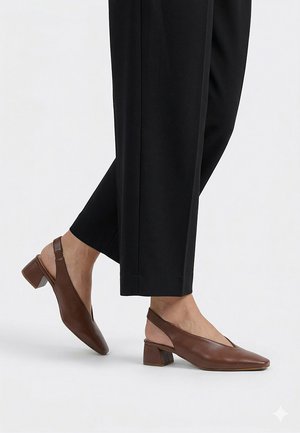 Zapatos slingback de cuero marrón con tacones bajos de bloque, usados con pantalones negros recortados sobre un fondo blanco liso.