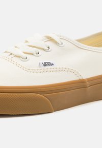 Sneakers di tela color crema con suola in gomma naturale, dotati di lacci bianchi e di un piccolo logo nero Vans sul lato.