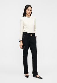 Μπεζ μακρυμάνικη μπλούζα με μαύρο περίγραμμα, συνδυασμένη με ψηλόμεσο μαύρο παντελόνι με χρυσή ορθογώνια αγκράφα. Μαύρες μυτερές μπαλαρίνες και τσαντάκι.