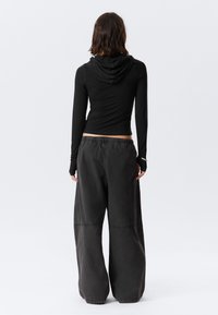 Sort langærmet top med hætte, tætsiddende ved taljen. Kombineret med løse, vidde bukser i mørkegrå, med elastik i taljen og synlige syninger.