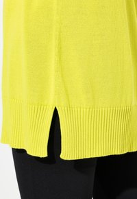Maglione lavorato a maglia giallo brillante con orlo a costine e spacchi laterali. La vista ravvicinata mette in risalto la texture e il colore, con una finitura liscia.