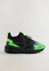 Sneaker nera con un accento verde sfumato, materiale testurizzato, suola flessibile e un design chiazzato di verde. Presenta il logo 'Minecraft' sul lato.