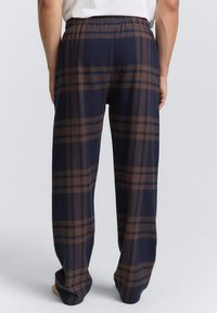 Marineblauwe geblokte broek met een relaxte pasvorm, elastische tailleband en een bruin ruitpatroon. Gemaakt van zachte stof, biedt het comfort en bewegingsvrijheid.