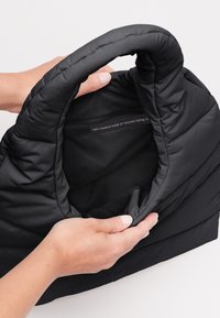 Czarna torba izolacyjna wykonana z recyklingowych sieci rybackich, z miękką zewnętrzną powierzchnią, zaokrąglonym wierzchem i wewnętrzną metką informującą o materiale.