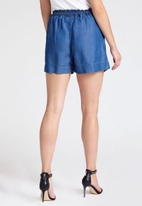 Shorts de mezclilla con cintura elástica, dobladillo vuelto y una longitud hasta medio muslo. Llevados con zapatos de tacón negro, con una correa en el tobillo.