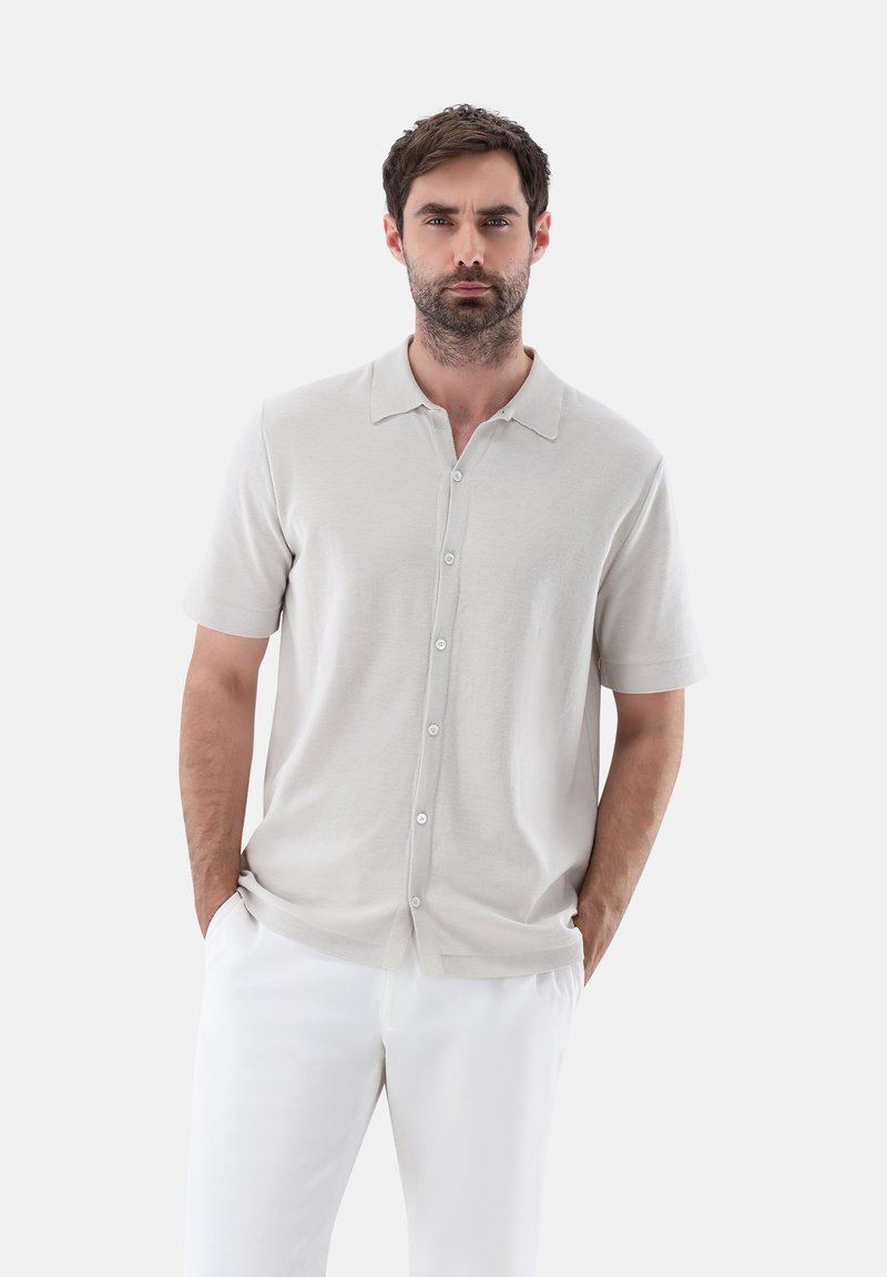 Camicetta grigia chiara a maniche corte con bottoni, realizzata in tessuto morbido, con colletto e chiusura frontale a bottoni. Abbinala a pantaloni bianchi.