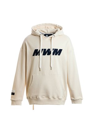 Persona joven con cabello rubio lleva una sudadera con capucha color crema, pantalones cortos deportivos blancos con rayas de colores, calcetines blancos y zapatos beige texturizados sin cordones.