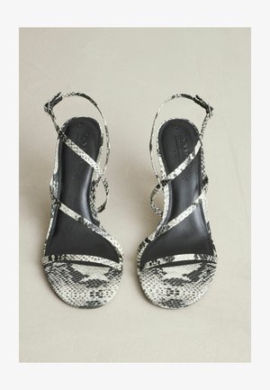 Sandale cu toc înalt, cu imprimeu de șarpe alb-negru, cu bretele împletite și o tălpă interioară netedă, neagră, căptușită.