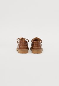 Chaussures en cuir marron avec une forme arrondie, à lacets et semelles en caoutchouc. Présentent des coutures blanches et une finition lisse.