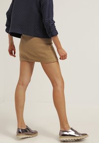 Veste en cuir matelassée bleu marine, mini-jupe beige, baskets métalliques brillantes. Accent sur des lignes épurées, des tissus texturés et un design moderne et décontracté.