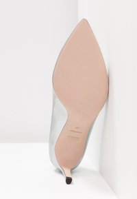 Chaussure à talon haut argentée avec un bout pointu et un design courbé, dotée d'une texture lisse et d'une semelle beige avec empreinte de logo.