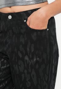 Crne traperice s teksturiranim uzorkom leopard printa, s bočnom džepom, metalnim gumbom i elegantnom završnom obradom tkanine.