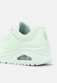 Ljusgrön träningsskor med en slät yta, perforerade detaljer och en vadderad häl med en synlig luftkammare i sulan.