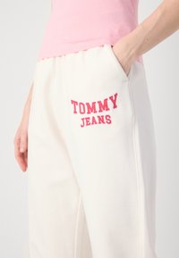 Witte trainingsbroek met een roze geborduurd "TOMMY JEANS" logo op de linkerzak. Zacht materiaal, comfortabele pasvorm, met zijzakken en een elastische tailleband.