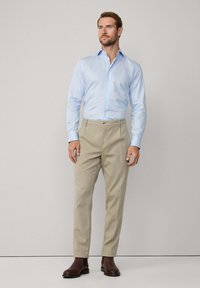 Light blue button-up shirt with long sleeves, paired with beige trousers and brown leather ankle boots. Smooth fabric and tailored fit.