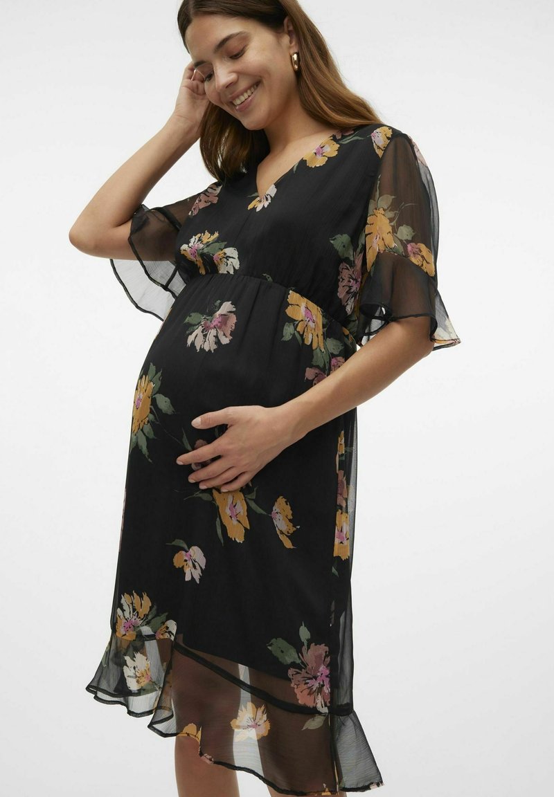 Zwart bloemenjurk met korte, semi-doorschijnende mouwen, V-hals en uitlopende zoom. Bevat gele, roze en groene bloemenpatronen op zachte stof.
