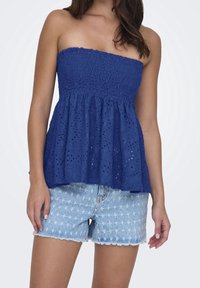Top azul marino sin tirantes con cuerpo texturizado y fruncido, y peplum acampanado; combinado con pantalones cortos de mezclilla clara con estampados de estrellas.