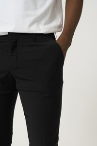 Czarne eleganckie spodnie wykonane z gładkiego materiału, w fasonie slim fit, z bocznymi kieszeniami i płaskim przodem. Noszone z białą koszulą.