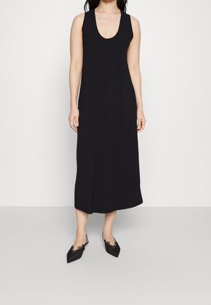 Robe noire sans manches en tissu doux, dotée d'un décolleté arrondi et d'une coupe décontractée, tombant jusqu'au mollet. Portée avec des chaussures noires à talons pointus.