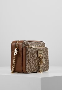 Hnědá kožená crossbody taška s béžovým vzorovaným plátnem vpředu. Obsahuje zlaté kovové detaily, zipový uzávěr a řetízkový popruh.