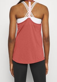 Punainen urheilullinen toppi, jossa valkoinen sisäkerros, ristitetyillä olkaimilla ja pyöristetty helma. Valmistettu kevyestä, hengittävästä materiaalista.