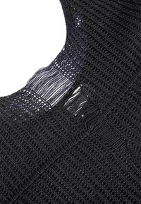 Tessuto all'uncinetto nero con trama aperta, caratterizzato da un motivo testurizzato e bordi frangiati, che mostra una piccola lacerazione nel materiale.