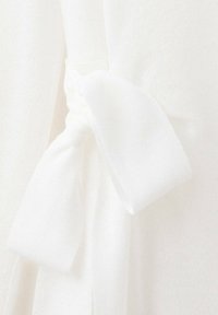 Tissu blanc doux noué en un nœud sur un vêtement, montrant la texture et les plis du matériau.