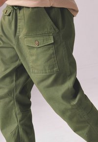 Grüne Cargo-Hose aus strapazierfähigem Stoff mit lockerer Passform, ausgestattet mit einer Seitentasche und flachem Bund, akzentuiert durch einen Knopfverschluss.