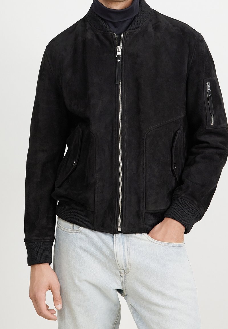 Giubbotto bomber in suede nero con zip frontale, polsini e orlo a coste, tasche laterali e tasca con zip sulla manica. Texture liscia, vestibilità moderna.