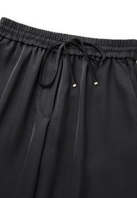 Zwarte drawstring broek met een elastische tailleband, een gladde textuur en een subtiele glans. Inclusief zijzakken en accenten in goudkleurige hardware.