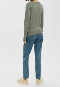 Pull vert en maille à manches longues et col rond, associé à un jean bleu taille haute et des baskets beige clair.