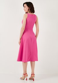 Fitted pink dress with a flared skirt, sleeveless design, and a hidden zipper at the back. Worn with strappy heeled sandals.