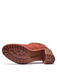 Bruine suède laars met een gestructureerde rubbere zool, voorzien van een uitgesproken profiel en een gebogen hak voor extra stabiliteit.