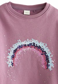 Vaaleanpunainen huppari, jossa on koristeellinen sateenkaari design sinisen, vaaleanpunaisen ja violetin sävyissä, teksturoidulla pinnalla ja ribbireunuksella.