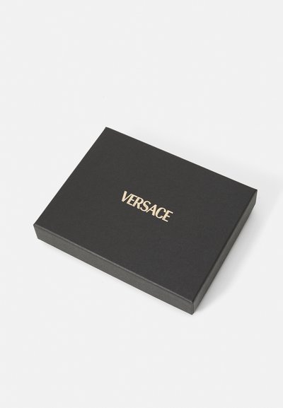 Must must kandiline kast, mille peal on kuldne "VERSACE" logo, valmistatud tekstuurilisest materjalist. Lihtne disain, millel ei ole täiendavaid mustreid ega aksessuaare.