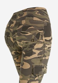 Pantaloni cargo mimetici in tonalità di verde e marrone, con un design aderente, tasche con chiusura a pattina e dettagli di cucitura in evidenza.