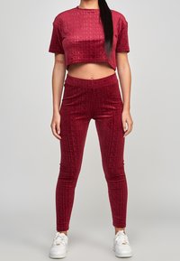 Top corto carmesí y leggings hechos de una suave tela texturizada con un patrón de logotipos repetido. Conjunto estilizado con zapatillas blancas.