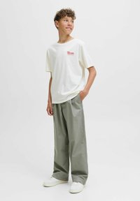 Crème katoenen t-shirt met rode print, gecombineerd met lichtgroene, losse broek en witte sneakers. Minimalistisch ontwerp met een relaxte pasvorm.
