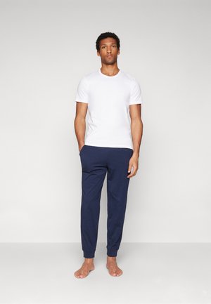 White cotton t-shirt with short sleeves paired with navy blue joggers, featuring elastic cuffs and pockets, on a bare-footed model.