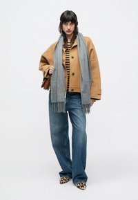 Veste marron oversize, haut à rayures, écharpe gris clair, jean large bleu et chaussures à imprimé léopard. Des accessoires simples complètent le look.