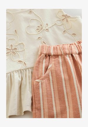 Blusa crema a maniche corte con ricamo floreale e orlo arricciato, abbinata a pantaloni a righe ruggine con fascia elastica in vita e tasche laterali.