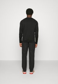 Svart långärmad tröja i strukturerad tyg med ribbade ärmslut och nederkant, kombinerad med svarta byxor och flerfärgade sneakers.